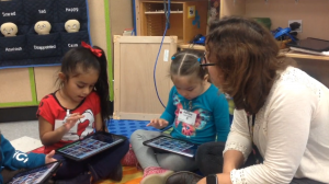 These children and their teacher in a bilingual preschool classroom are using an app to create a “story” with photos of their recent field trip.