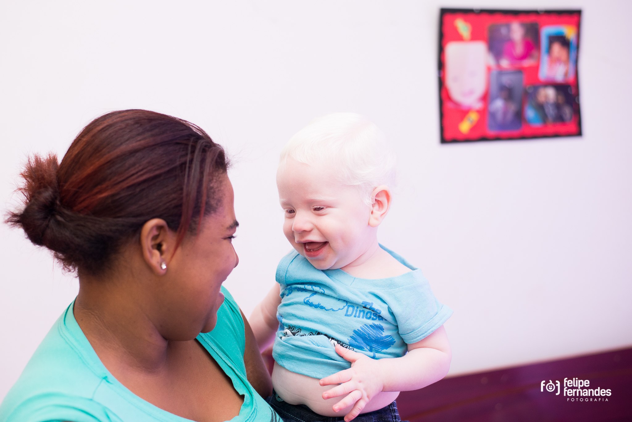 Image shows a young black woman holding and smiling at a delighted 9-month old albino baby.