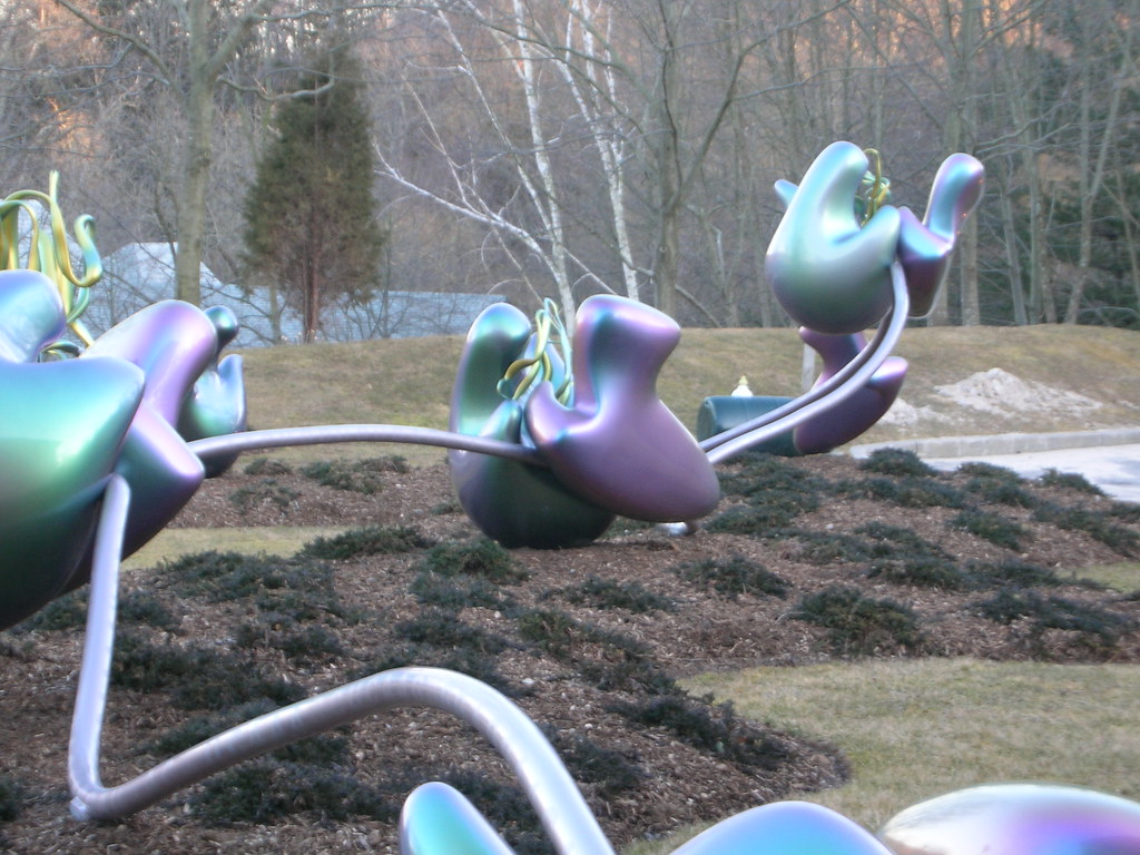 Image shows a large 3D work of art displayed at the Cold Spring Harbor Laboratory. It is a representation of ribosomes attached to a ribbon of metal meant to represent a strand of messenger RNA.