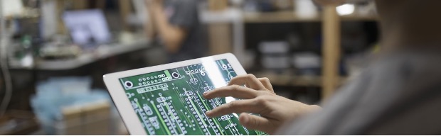 Close up of an engineer examining circuit board on digital tablet