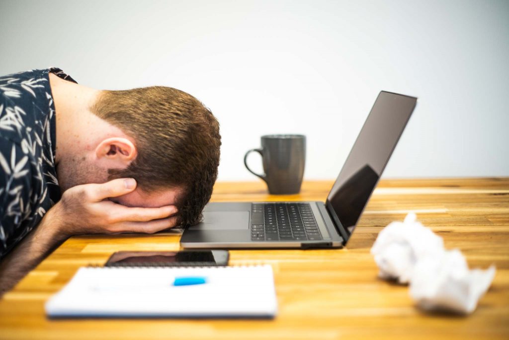 “Burnout_At_Work_-_Occupational_Burnout.jpg” by Microbiz Mag is licensed under CC BY 2.0 Photo showing a person with head on table, hands holding head, office supplies and laptop on table