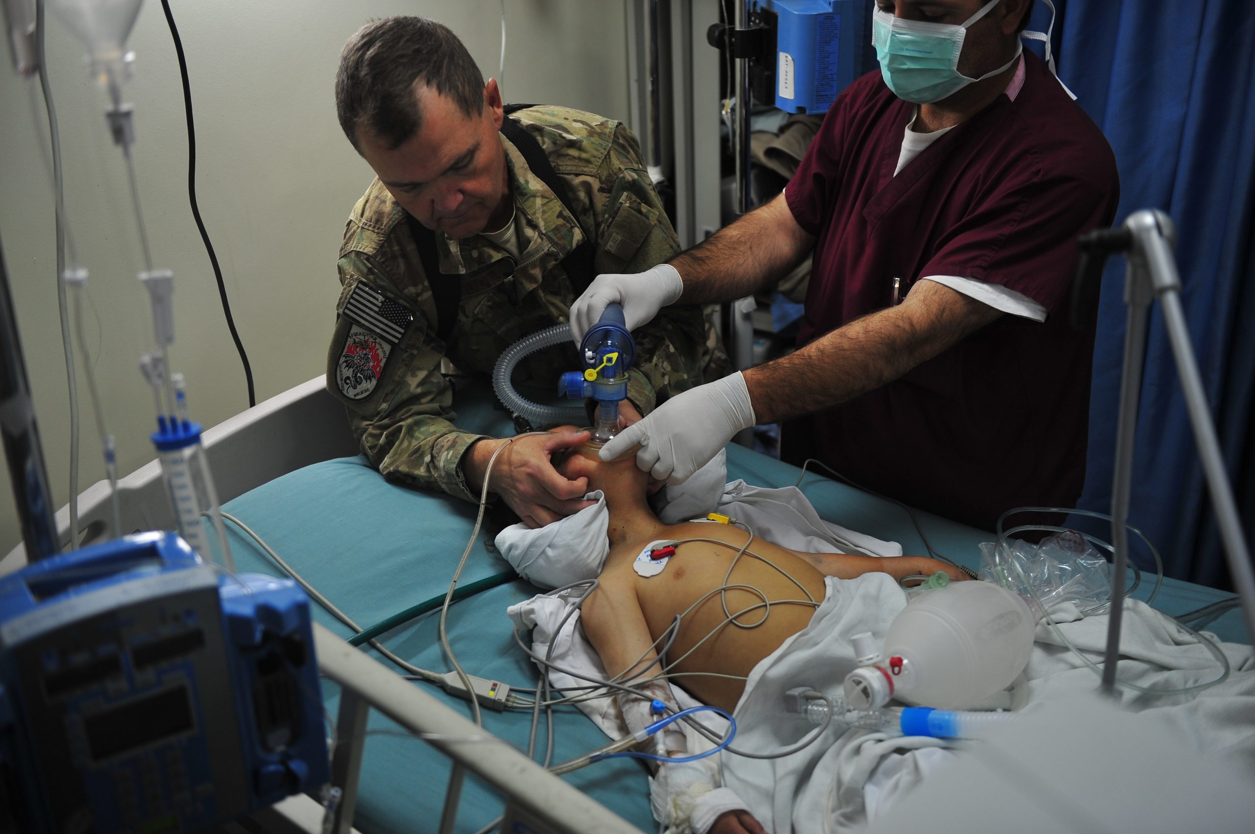 “Air_Force_special_operations_medical_team_saves_lives,_helps_shape_future_of_Afghan_medicine_111010-F-QW942-082.jpg” by Senior Airman Tyler Placie is in the Public Domain Photo showing an Air Force critical care nurse assisting a doctor in helping a child breathe