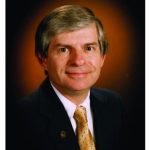 Headshot of white middle-aged man in suit and gold tie