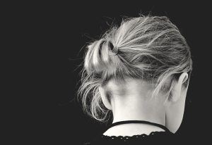 Black and white photo of back of girl's head. She is wearing black and her head is down, giving off a melancholy feeling