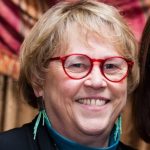 Middle aged white woman with short blonde hair and red glasses
