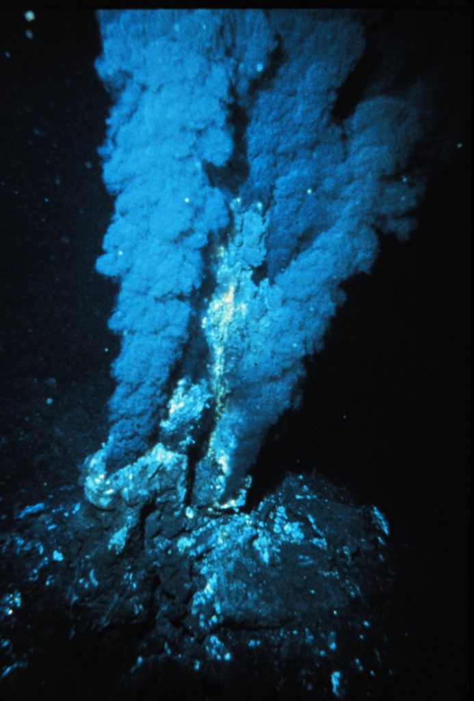 Photograph. A "black smoker" hydrothermal vent. The "smoke" consists of dissolved particles that precipitate into solids when exposed to colder water.