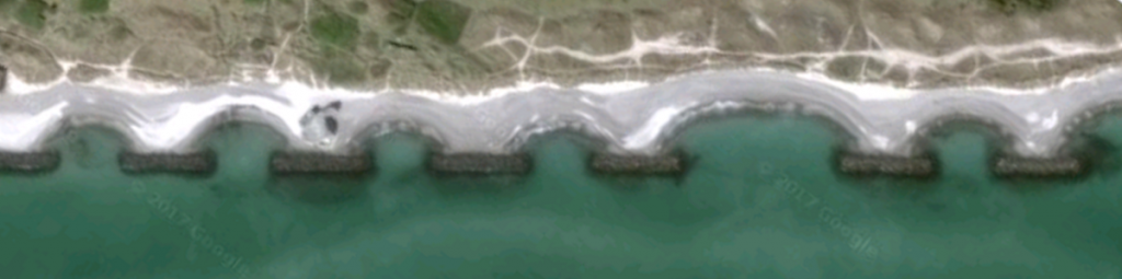 Image of a series of breakwaters along the coast in Skagen, Denmark. In this case, sand has accumulated to the point that they now connect the breakwaters to land