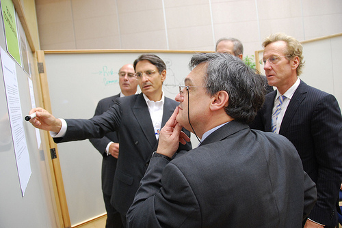 Photograph of business men considering document on whiteboard.