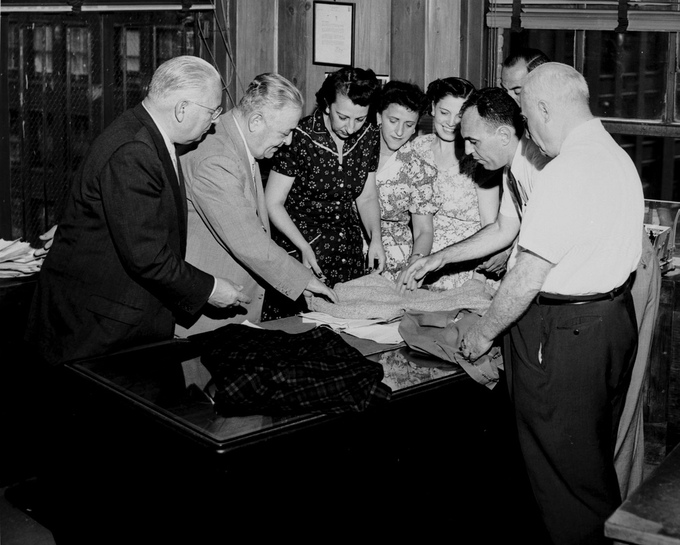 Black and White photograph of business men and women looking at textiles.