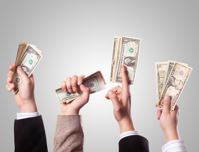 Photograph of four hands holding up various amounts of money.