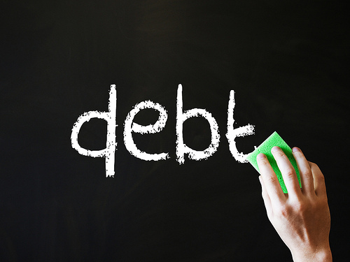 Image of the word debt written on black background in chalk being erased.