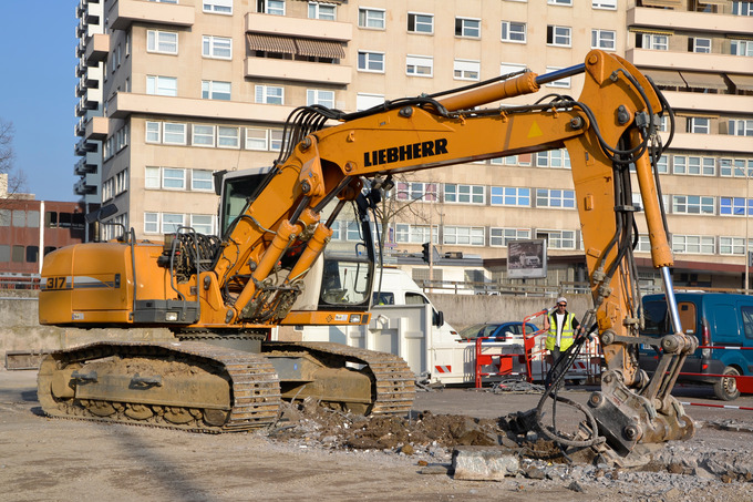 Image of an excavator breaking up asphalt on construction site.