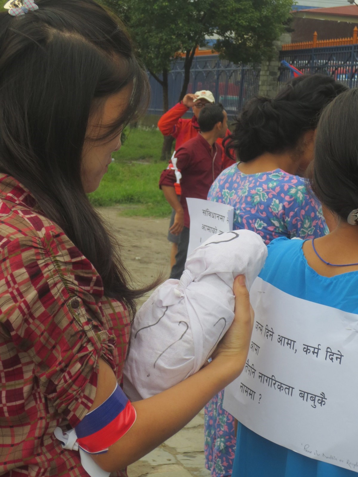 A young woman carries an effigy of a baby covered with question marks. The sign pinned to the back of the protester in front of her reads “Birth and karma are given by mothers.