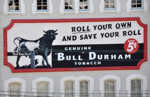 Billboard reading Roll Your Own and Save Your Roll Genuine "Bull Durham" tobacco.