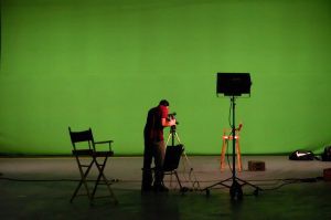 Photographer setting up camera shot in front of a green screen.