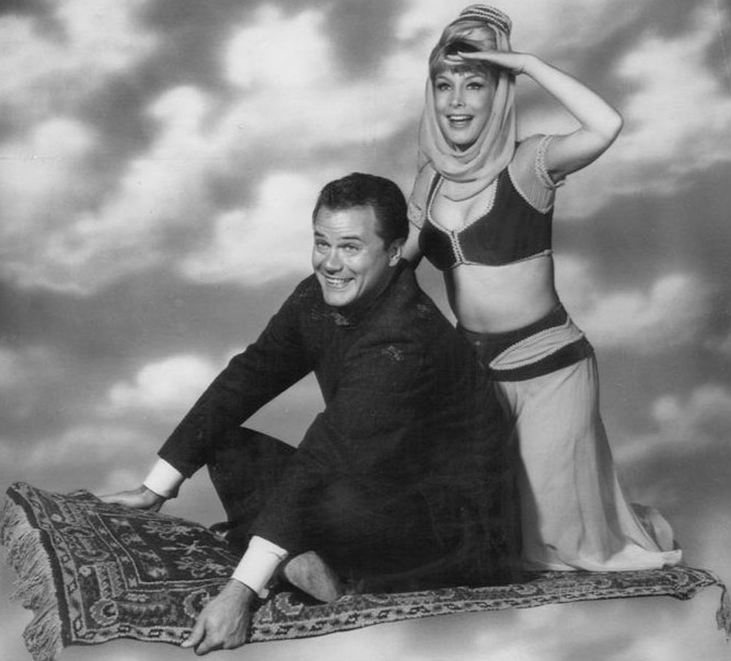 Larry Hagman and Barbara Eden sitting on flying carpet.