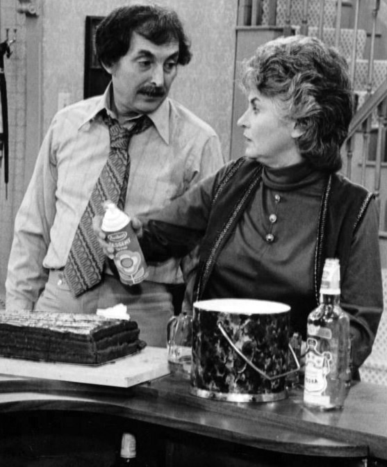 Bill Macy and Bea Arthur on the set of Maude. Bea Arthur is holding a can of whipped cream putting it on a cake.