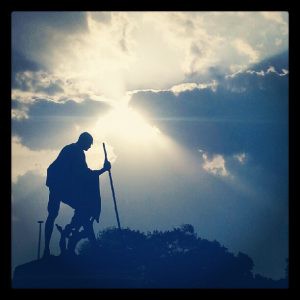Silhouette of Mahatma Gandhi with a sunray bursting through the clouds.