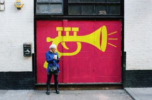 Person standing in front of a yellow trumpet painted on a red door.