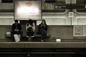 Three people sitting on a bench in a subway.
