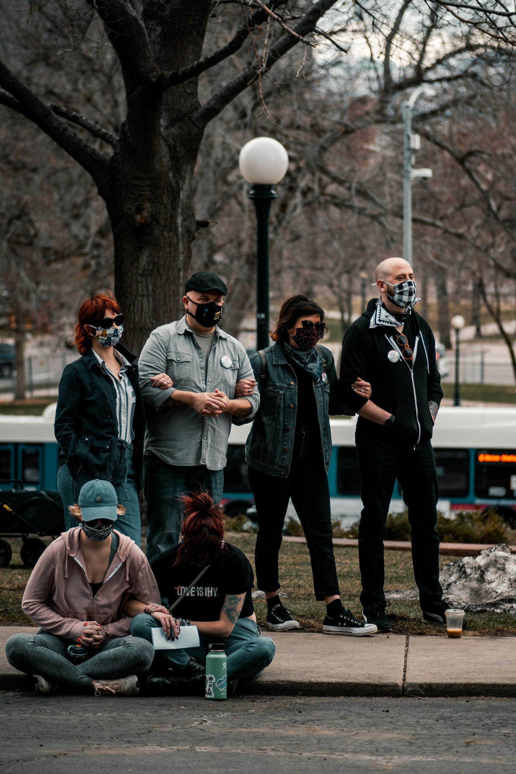 People wearing facemasks while standing on the street and sitting on a curb.