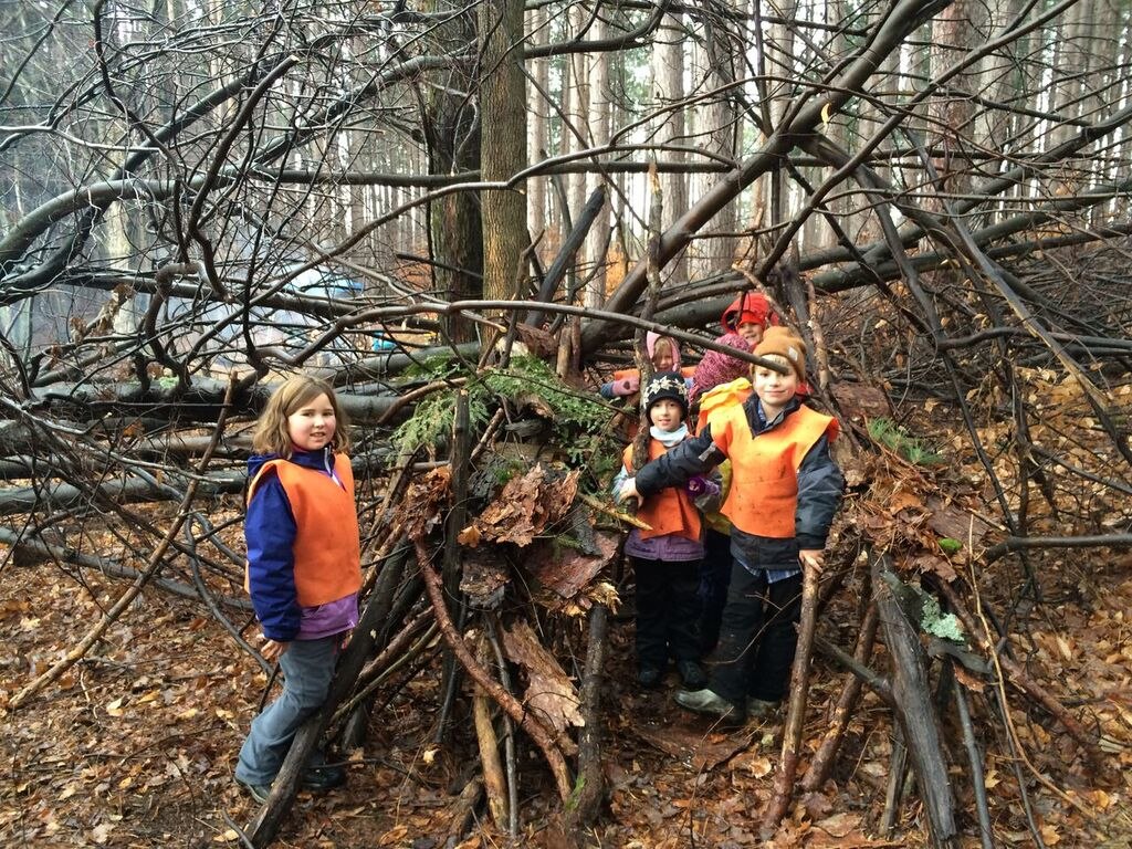 Children posing by created shelter in the woods.