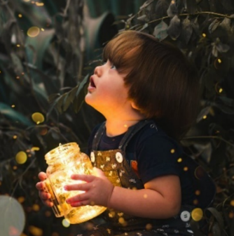 Young boy holding clear glass jar with yellow lights