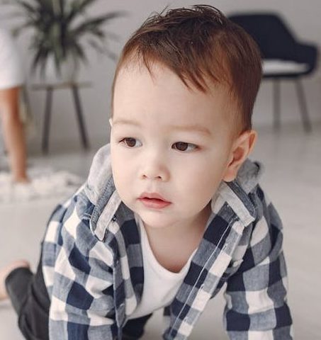 Toddler boy in a blue and white checkered shirt crawling.