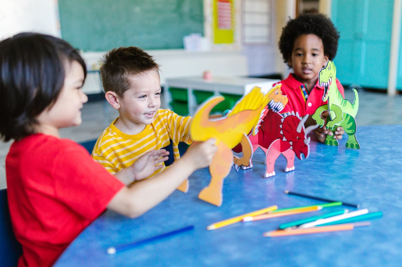 Three preschool students playing with paper colored dinosaurs.