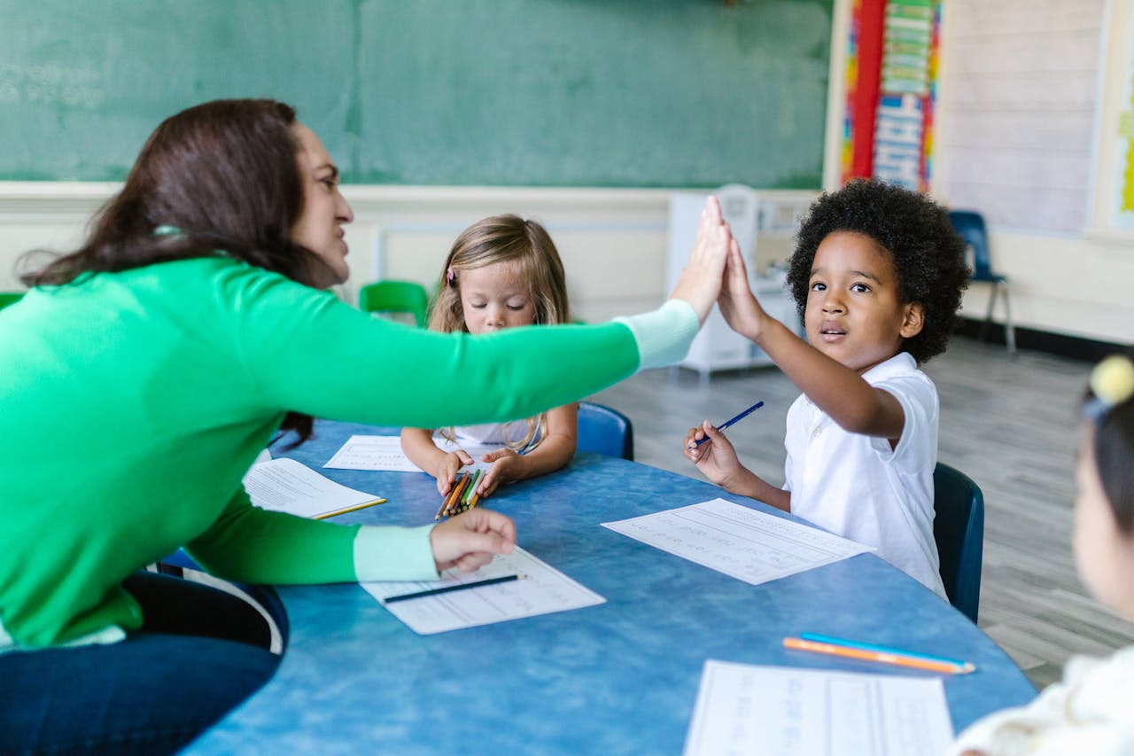 Teacher in a green sweater high fiving a student across the table.