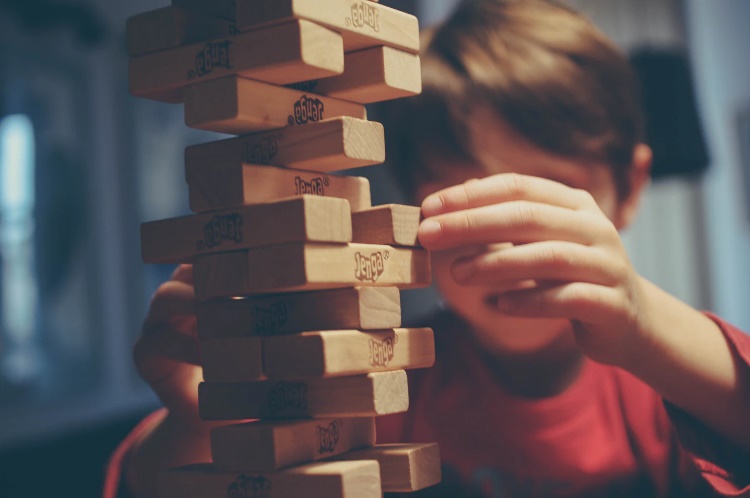 Young boy with brown hair wearing a red shirt playing Jenga.