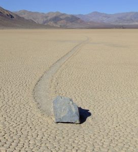 Sliding stone on flat desert with long trail.