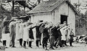 Photograph of school aged children who appear to be in Nazi Germany saluting a swastika flag or perhaps paying respect to a large poster of Adolf Hitler