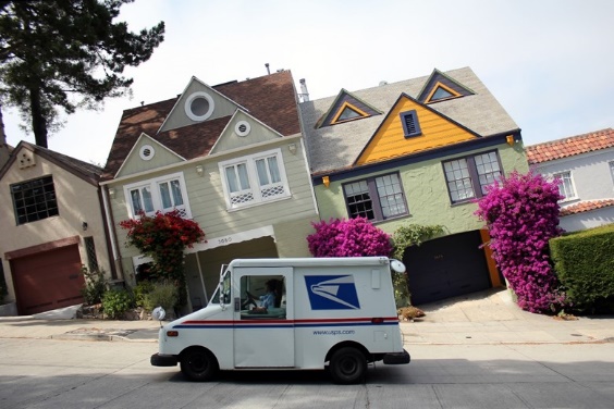 Mail truck parked in front of tilted houses.