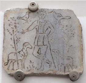 A marble slab with a crudely etched man, sheep and birds.