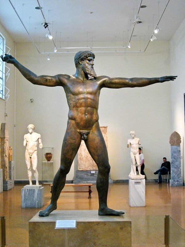 Bronze statue of a nude, bearded male with legs spread apart for a strong stance. He holds one hand out where he is looking and the other is stretched behind him as if he is throwing something.