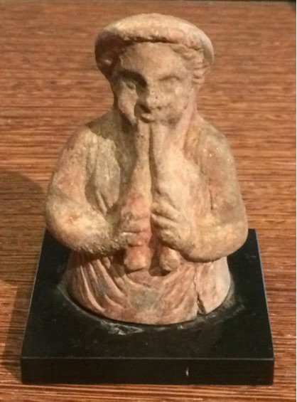 The top of a terra cotta (clay) statue of a man playing a double flute.