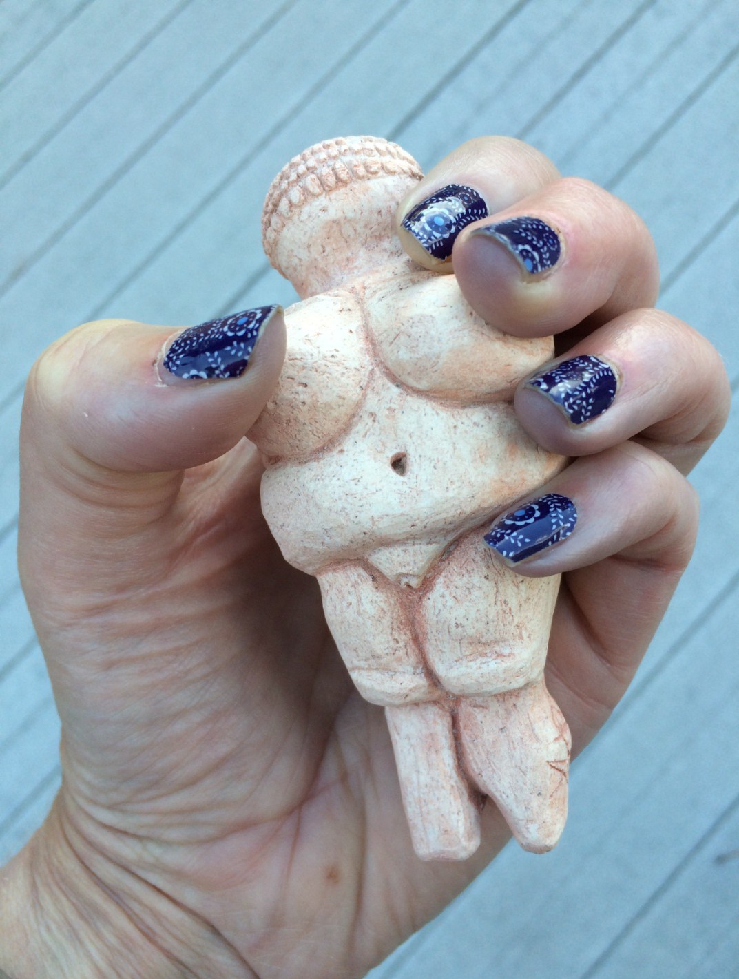 A hand holding a small stone figure of a woman with small arms and no feet or face.