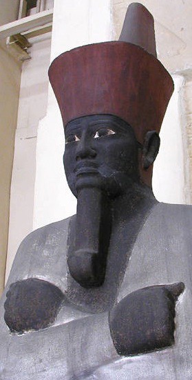Carved and painted statue of a seated Mentuhotep II. His skin is black, a symbol of a deceased being. His crown is red, and his clothing is white.