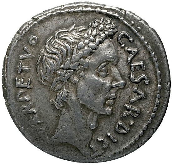 A silver coin with the head of a young man with writing around it.