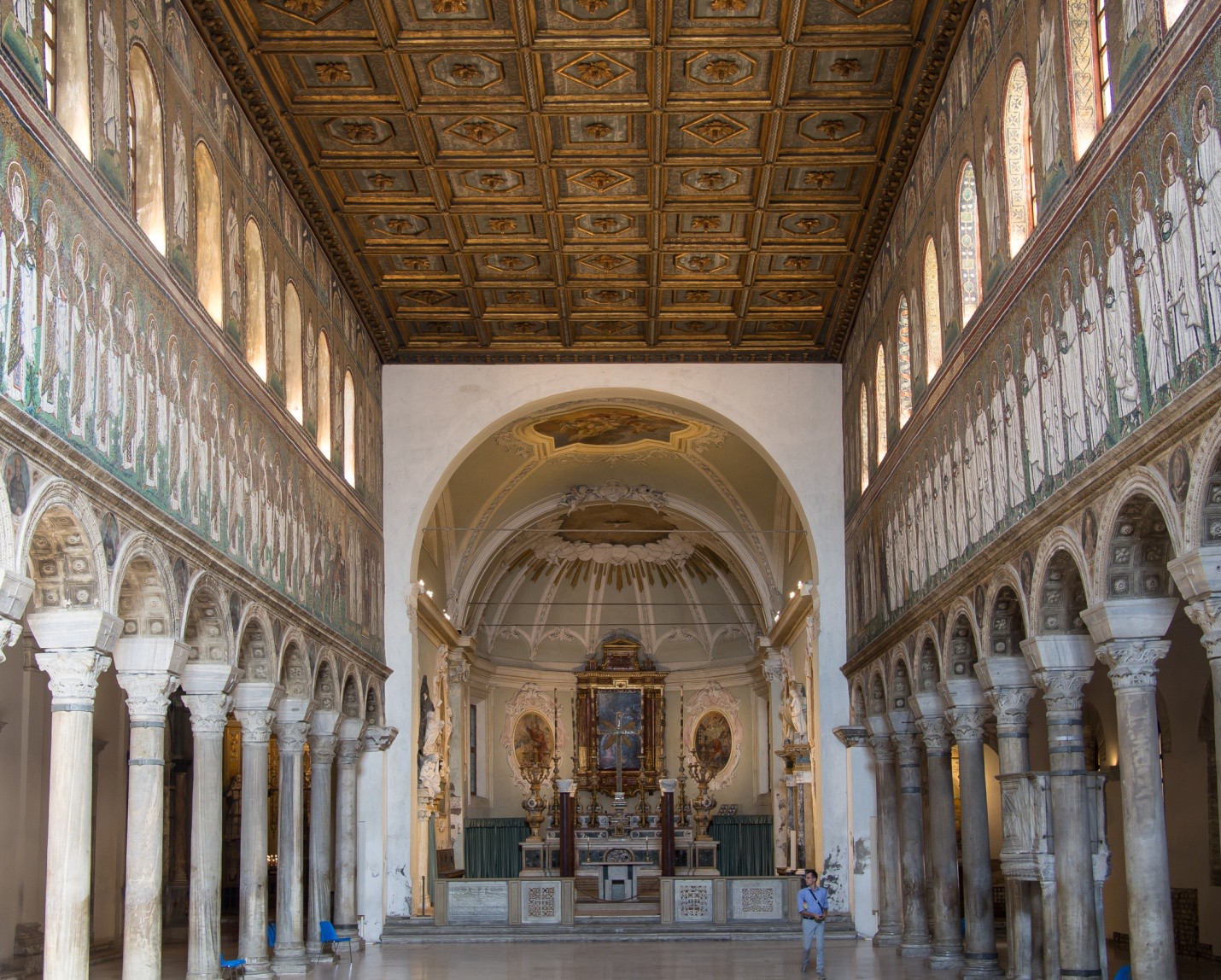 Apse seen from the front door. The ceiling is coffered and there are mosaics above the columns of the side aisles.