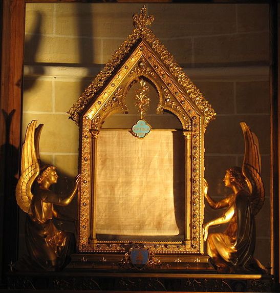 A miniature gold building flanked by an angel on each side and containing a piece of cloth.
