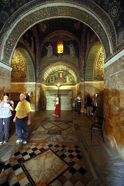 People walk through the mausoleum across a floor tiled in colored marble as they view the wonders above them.