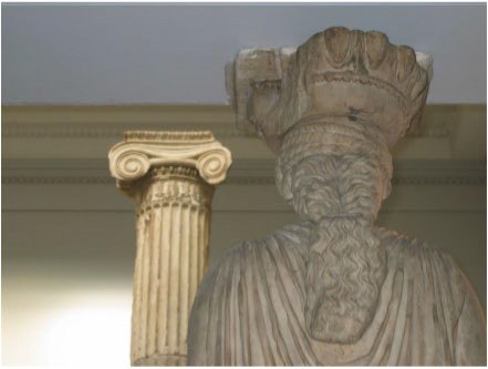 Rear view of a Caryatid, which is carved on all sides. Her thick, wavy hair is bound in a ponytail.