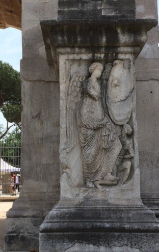 A winged figure stands on a small person.
