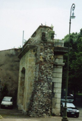 A photo of a piece of the remaining city wall. A car is parked on each side of it.