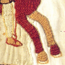A detail of a horse’s front hooves. A man’s foot is seen in a stirrup.