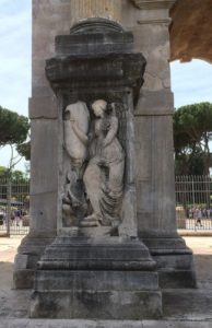 A winged figure stands on the leg of a person who seems to be trying to rise.