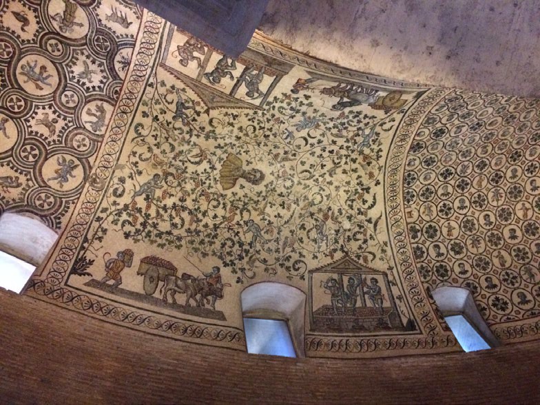 A detailed mosaic with an image of a girl in the center. Around her are grape leaves and a scene of everyday life with oxen, carts and gazebos.