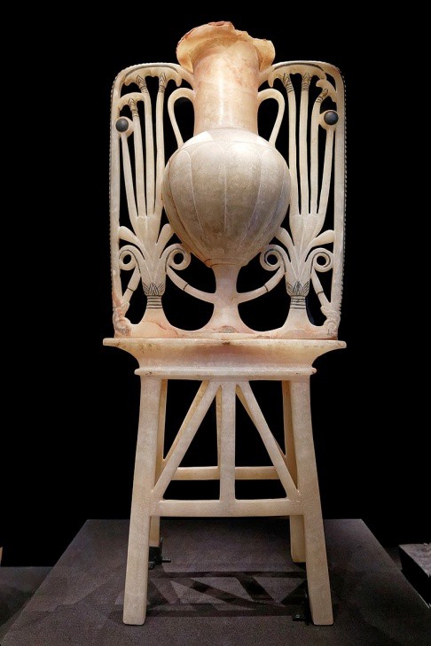 An unguent jar carved from alabaster that includes an elaborate stand that resembles a chair.